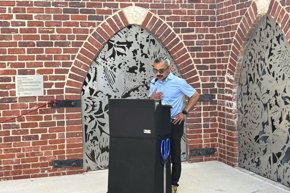 Artist Samson Barboza speaks at the Parque Zaragoza Bathhouse ribbon-cutting ceremony on June 10 in East Austin. His stainless steel sculpture, Brown Birds (left) Grackle (right) (2025), is visible behind him. (Jessica McLaren/Community Impact)